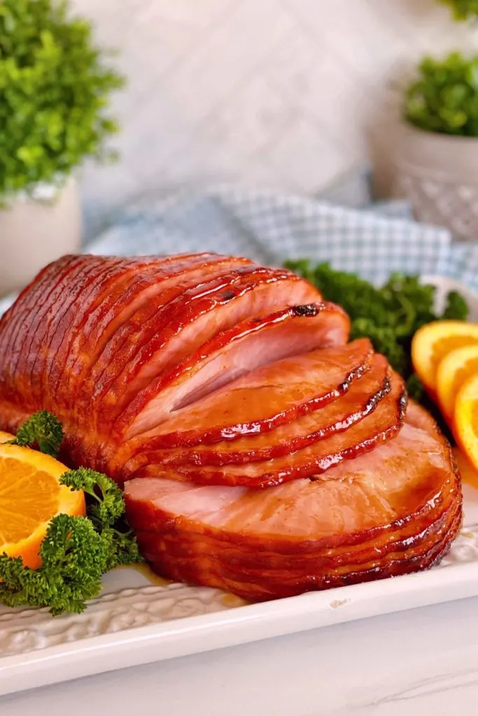 Whole Dr Pepper Glazed Spiral Ham on a serving platter surrounded by parsley and sliced oranges.