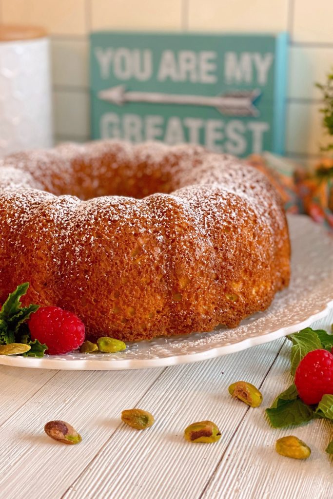 Pistachio Bundt Cake on white serving plate with raspberries.