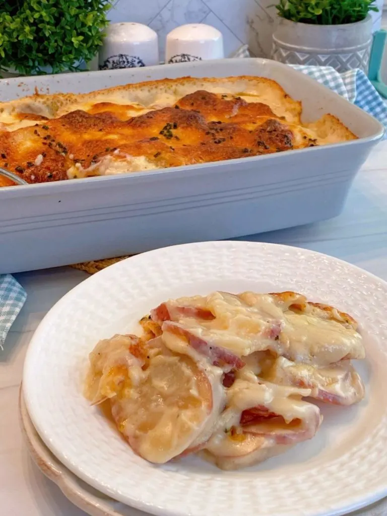 Creamy Cheesy Au Gratin Red Potatoes in a casserole dish with a serving on white plates stacked.