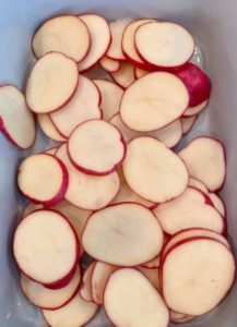 Placing a layer of thinly sliced red potatoes in the bottom of a baking dish.