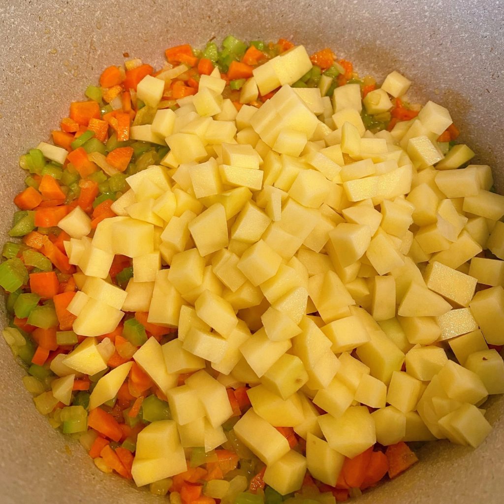 Adding potatoes to carrot and celery mixture for clam chowder.