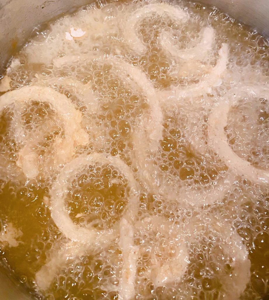 Onion rings frying in a sauce pan full of hot oil.