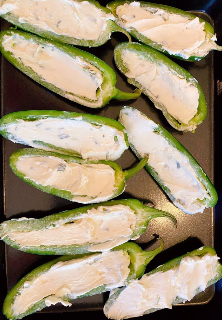 jalapeno peppers stuffed with cream cheese on a baking sheet.