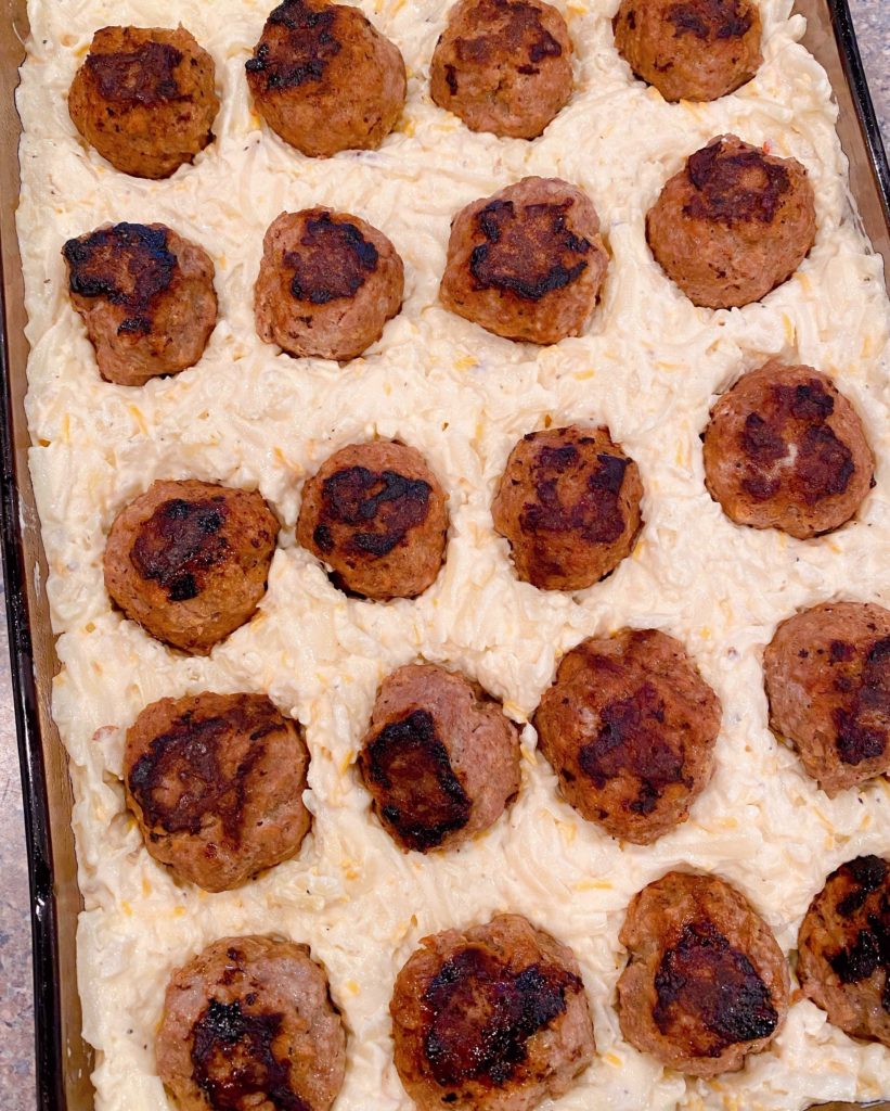 Meatballs pressed into potato mixture in baking dish.