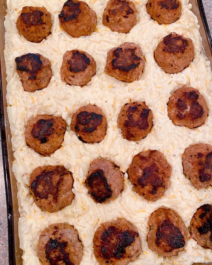 Meatballs pressed into potato mixture in baking dish.