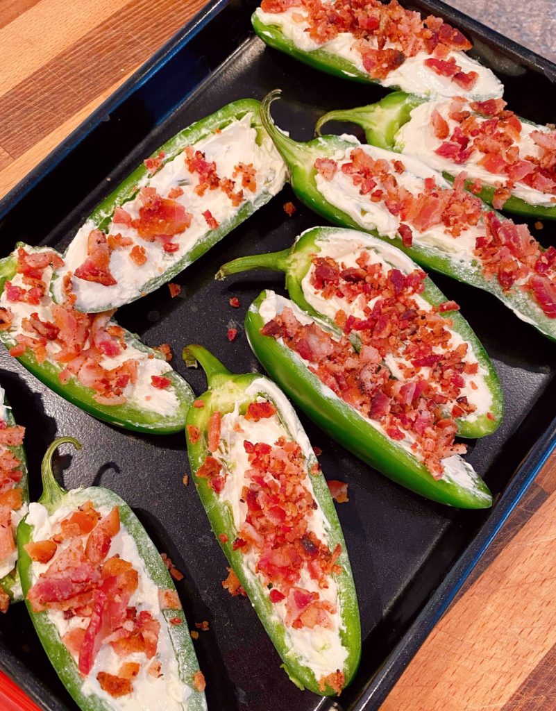 Jalapeno peppers stuffed with cream cheese and bacon crumbles on a baking sheet.