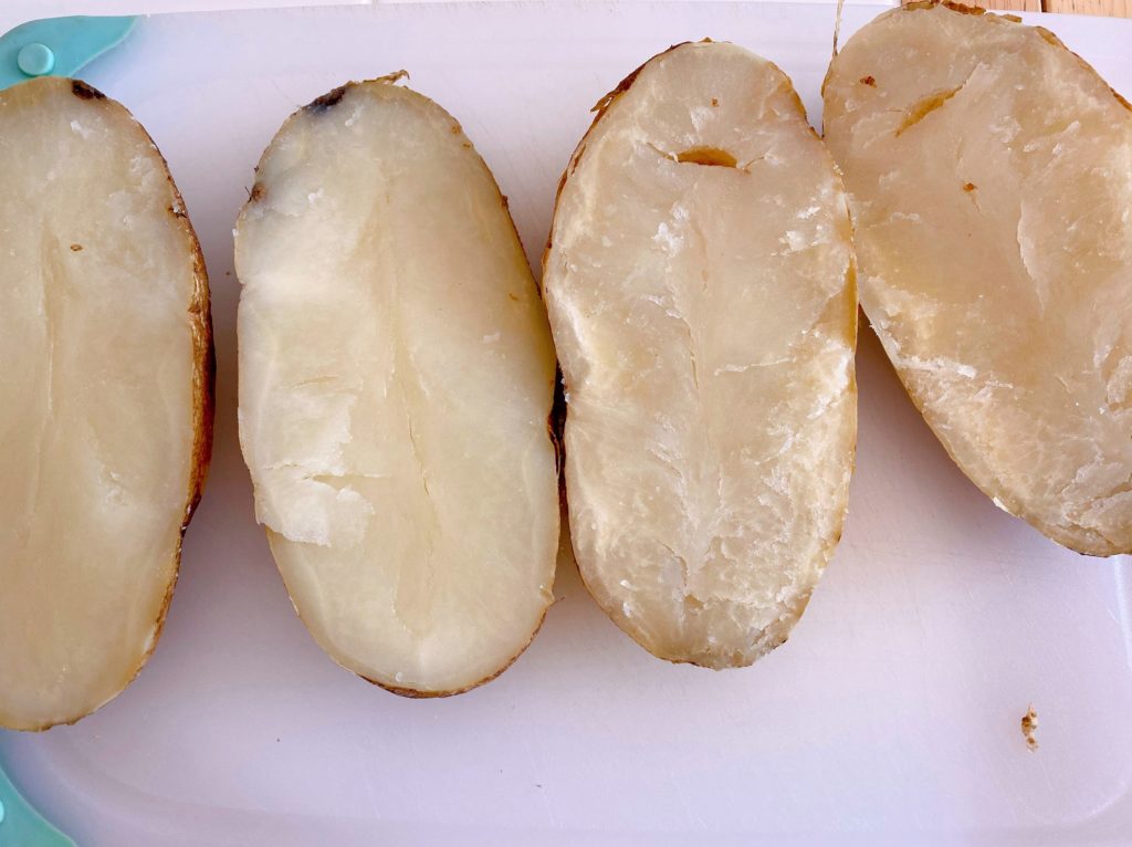 Baked potatoes cut in half length wise on a cutting board.