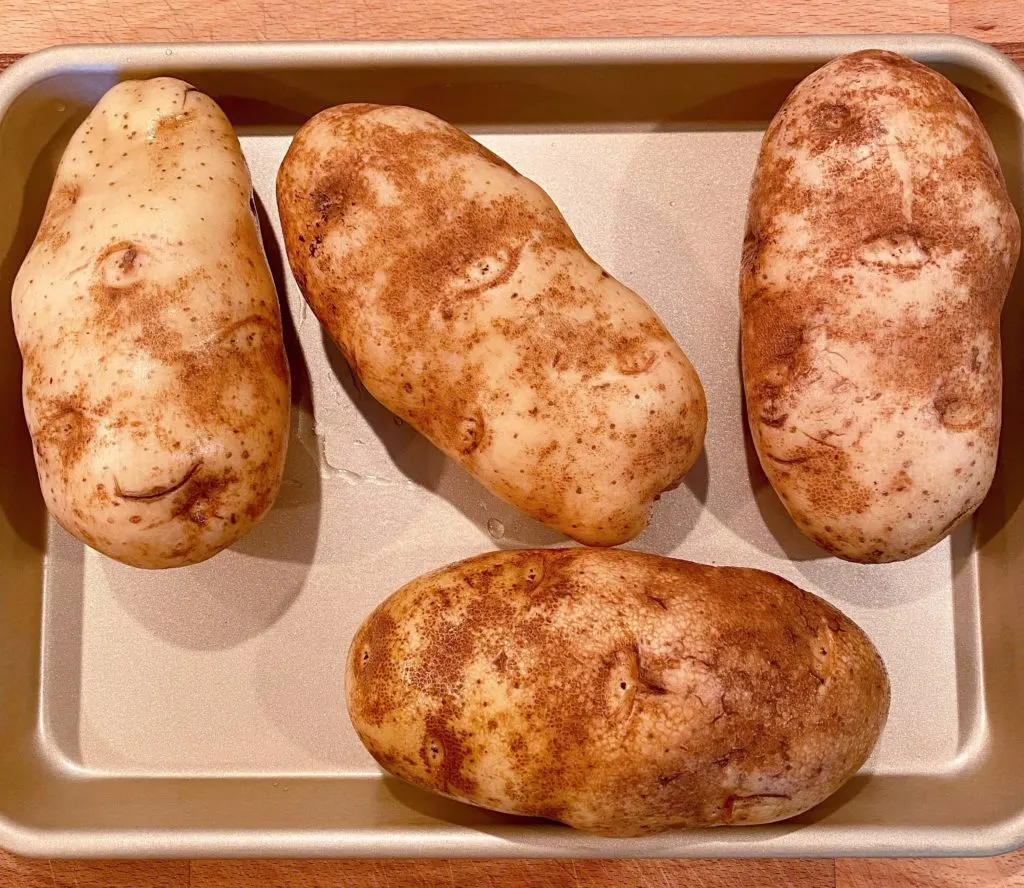 Washed baked potatoes on a baking sheet.