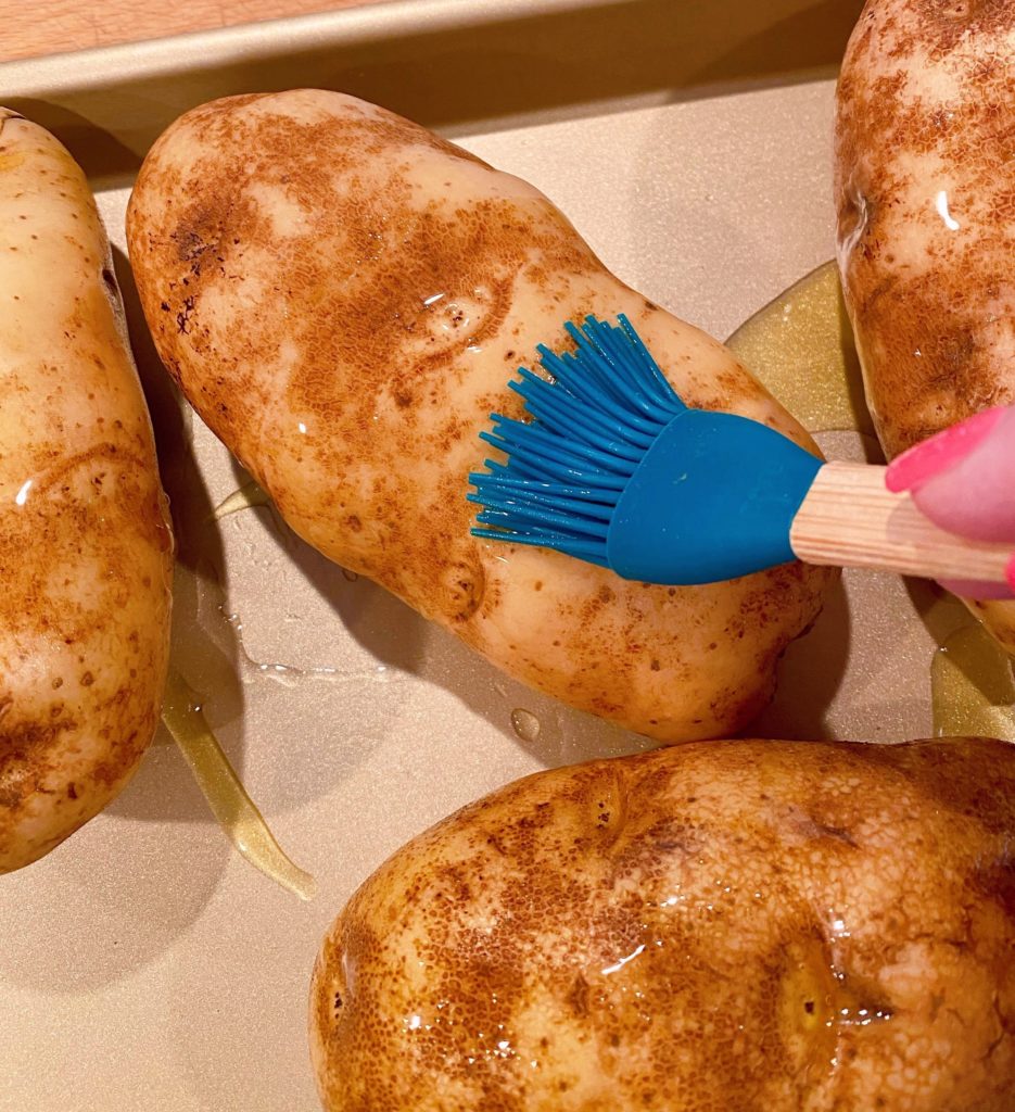 Coating potatoes with olive oil using a pastry brush.