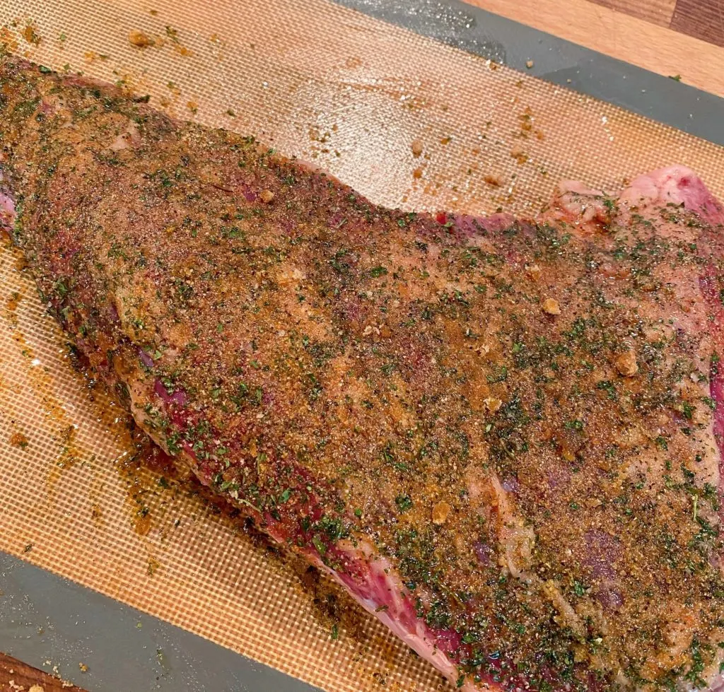 Tri-tip covered in seasoning rub on a cutting board.