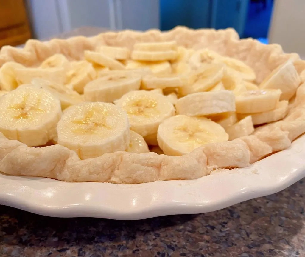 Bananas sliced and layered in the bottom of the pie crust.