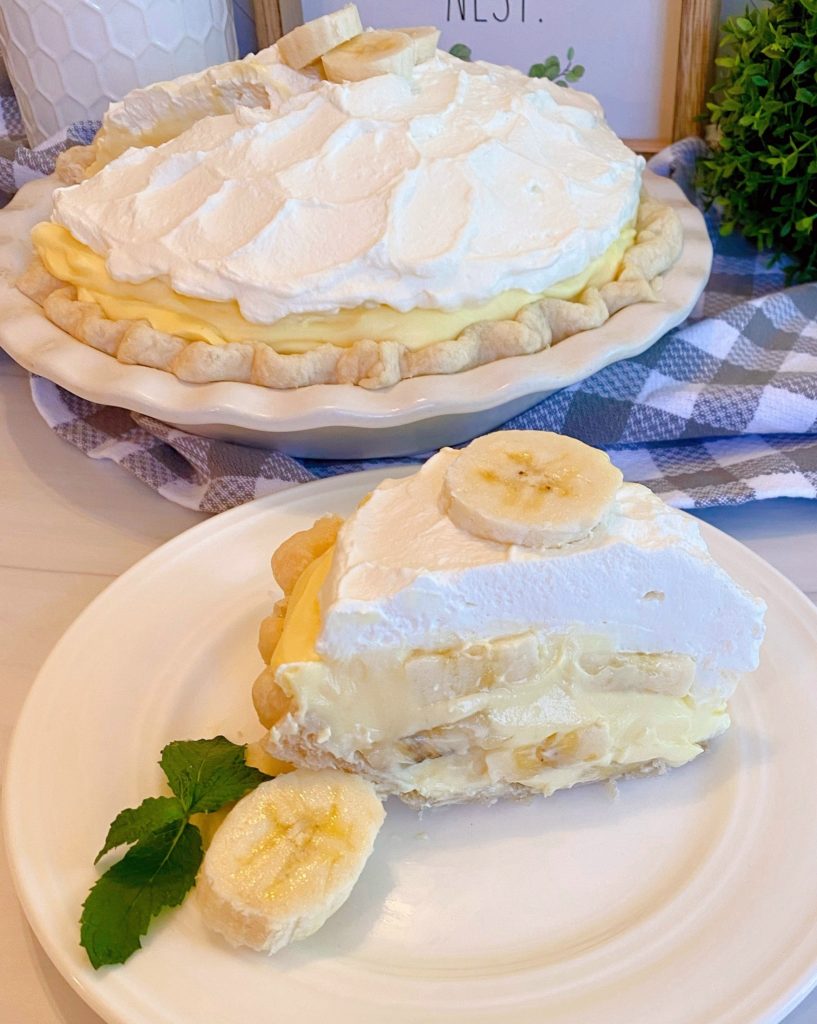 Banana Cream Pie with a slice on a white plate with sliced banana next to it and a sprig of mint.