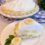 Banana Cream Pie with a slice on a white plate with sliced banana next to it and a sprig of mint.