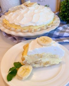 Banana Cream Pie with a slice on a white plate with sliced banana next to it and a sprig of mint.