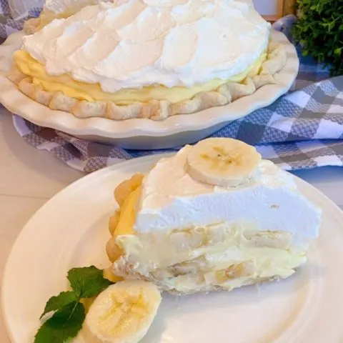 Banana Cream Pie with a slice on a white plate with sliced banana next to it and a sprig of mint.