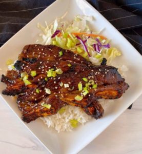 Hawaiian Style Short Ribs on a plate with rice and onion garnihs.
