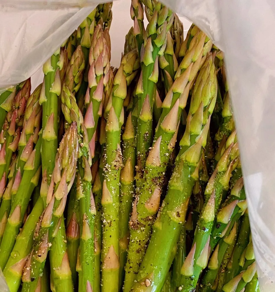 Asparagus spears in a large zip lock bag, drizzled with olive oil, and seasoned with salt and pepper.