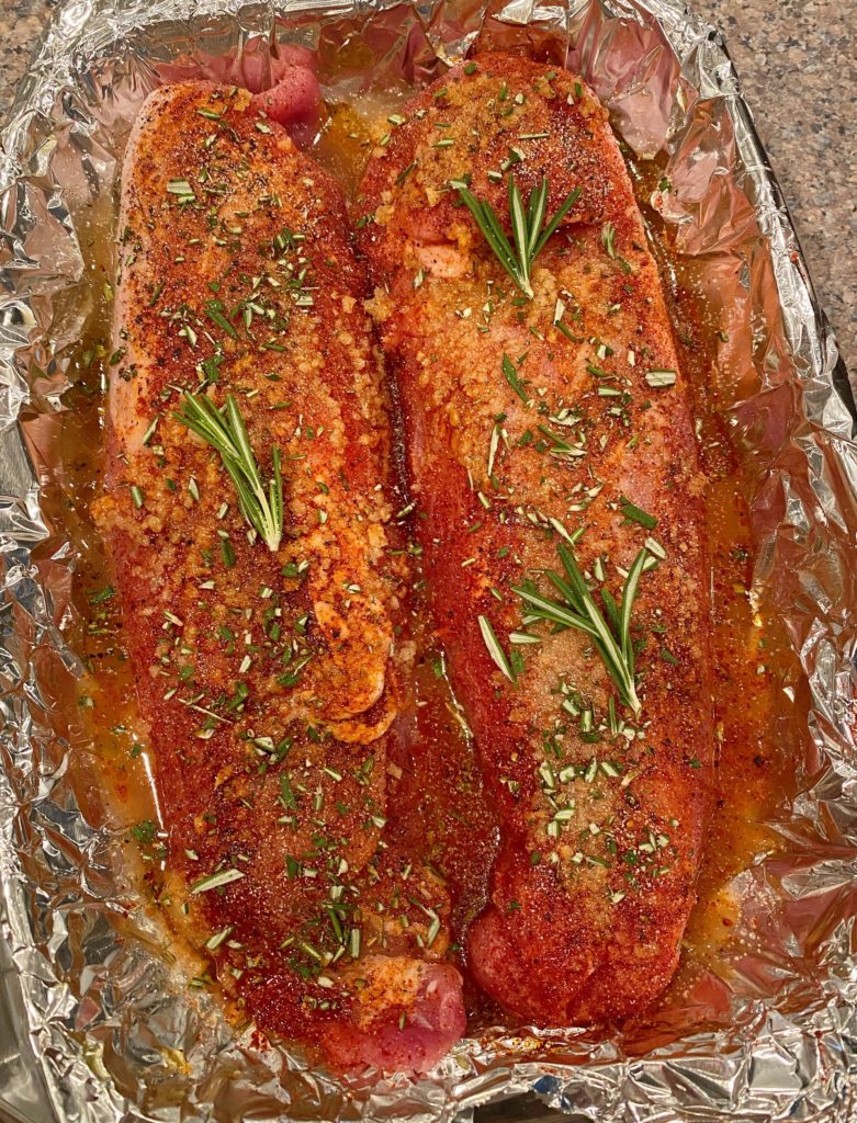 Pork Tenderloins in a lined baking dish covered with seasonings and sprigs of rosemary.