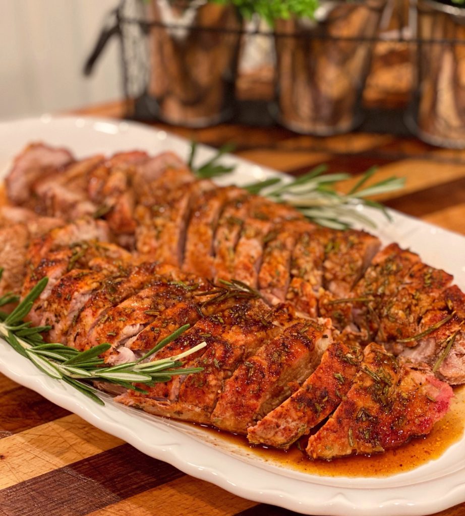 Easy Sliced Herb Crusted Pork Tenderloin on a white serving platter with a balsamic drizzle and sprigs of rosemary for garnish.