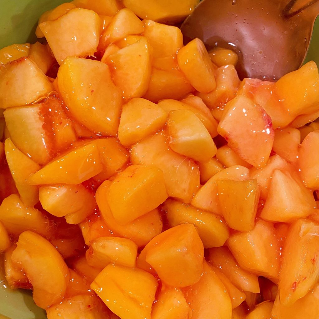 Bowl full of freshly peeled and sliced peaches with glaze over all of them ready for the pie shell.