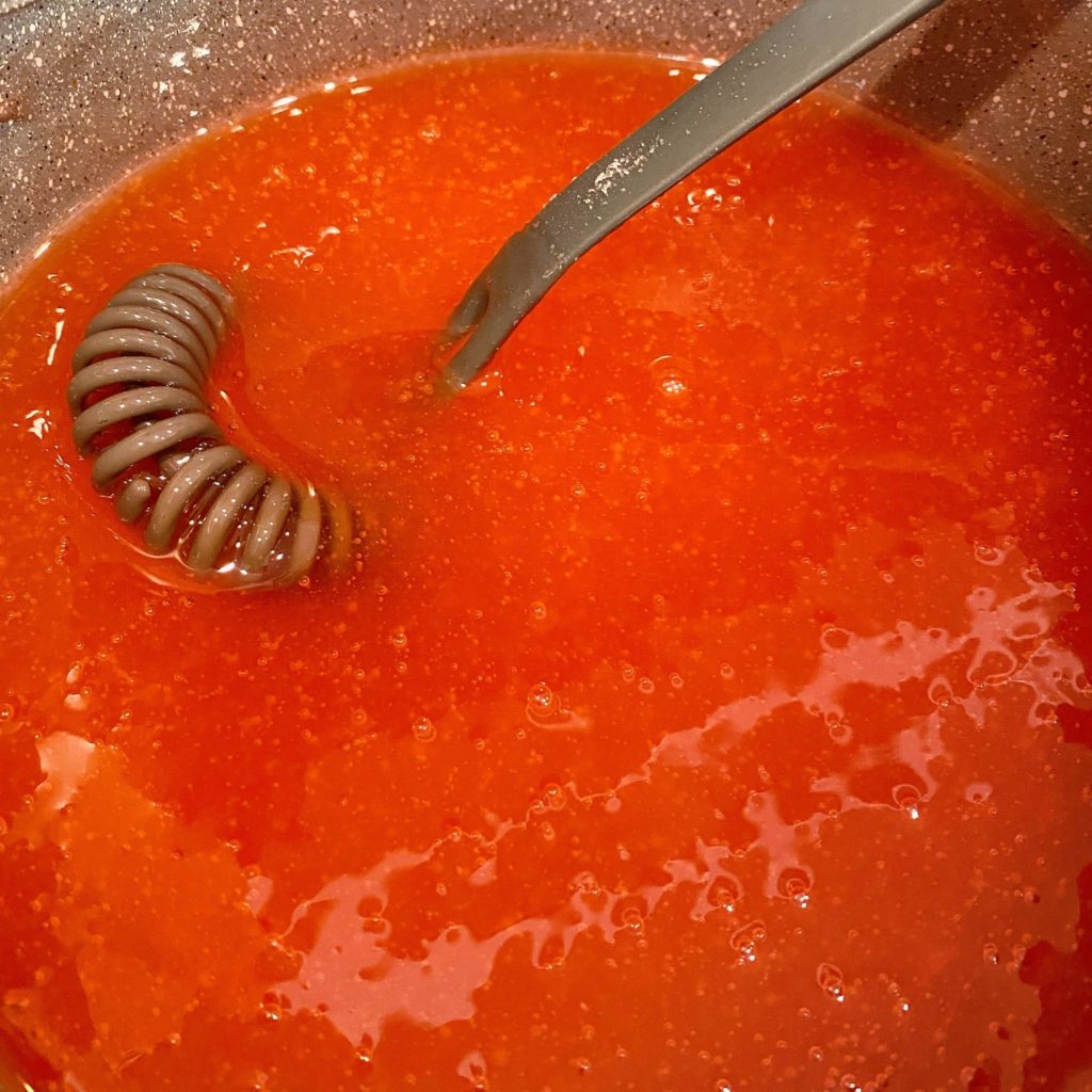 Peach glaze mixture in a pan with whisk cooling to add with peaches.