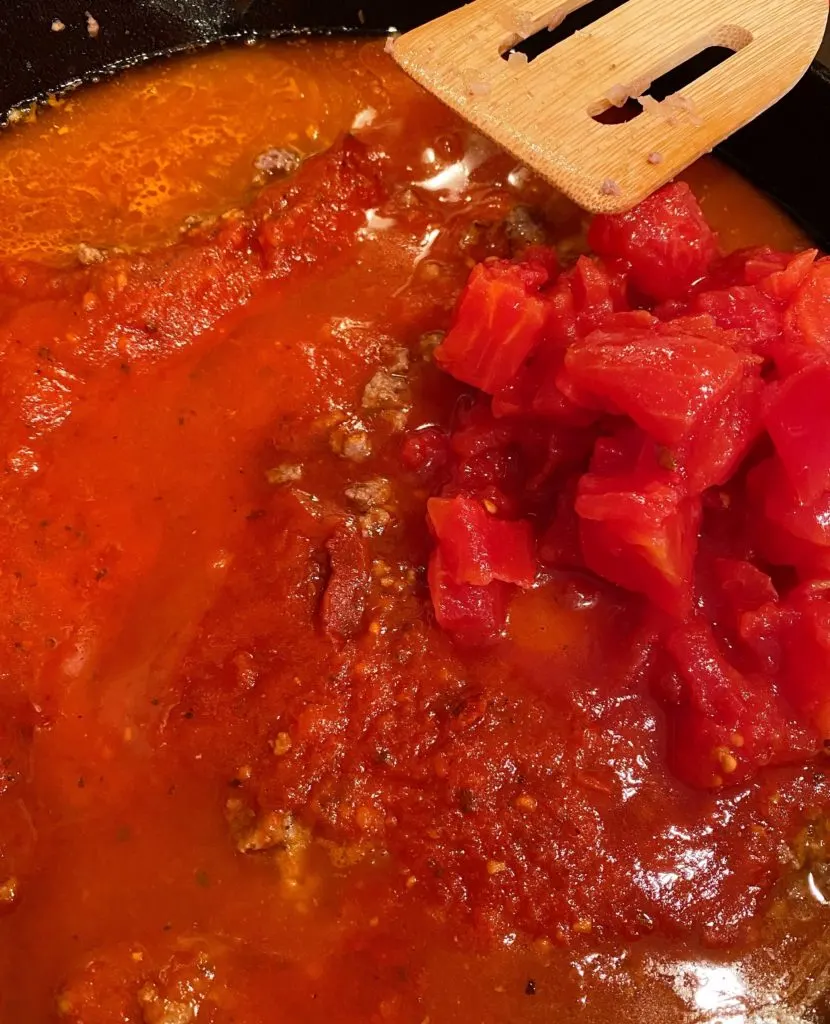 Adding sauce and water to ground beef in the skillet.