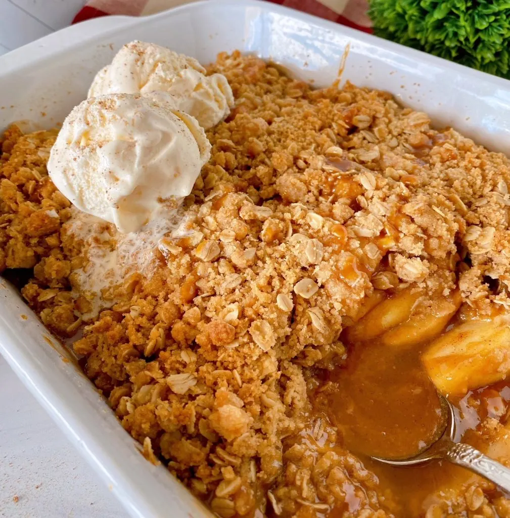 Apple Crisp Removed from oven and in baking dish with a serving removed and two big scoops of ice cream on top.