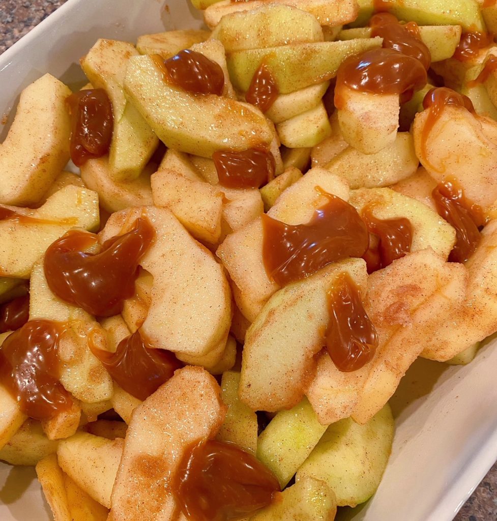 Apples in baking dish dotted with Caramel topping.