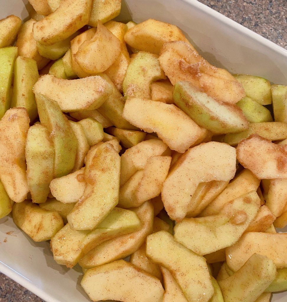Apples coated in sugar, flour, and cinnamon in a 9 x 13 baking dish.