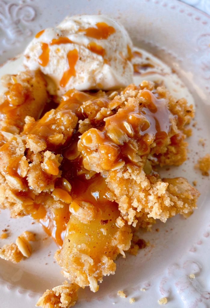 A serving of Caramel Apple Crisp with scoop of vanilla ice cream on a dessert plate.