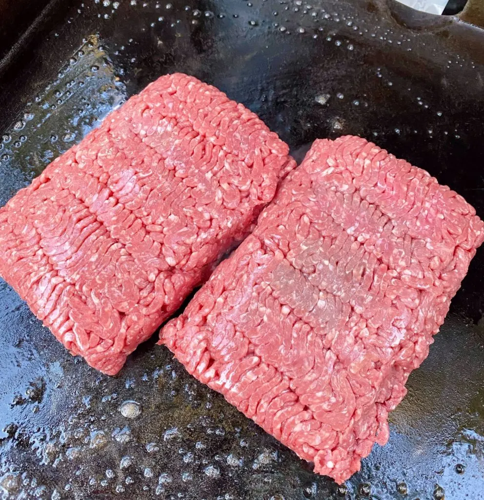 Two pounds of ground beef on hot black stone griddle.