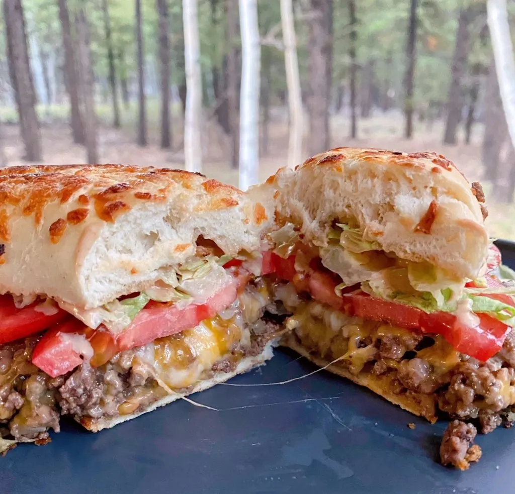 Loose Meat Sandwich Cut in half on a plate with the forest in the background.