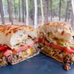 Loose Meat Sandwich Cut in half on a plate with the forest in the background.