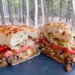 Loose Meat Sandwich Cut in half on a plate with the forest in the background.