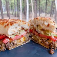 Loose Meat Sandwich Cut in half on a plate with the forest in the background.