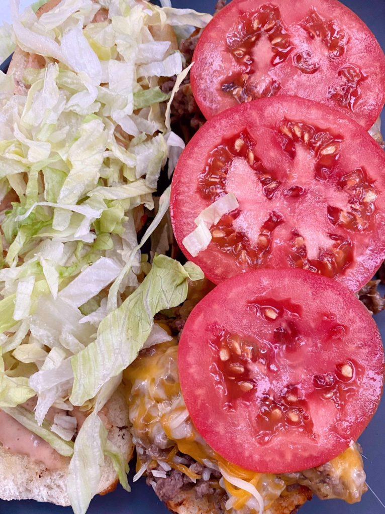 Adding tomatoes and lettuce to the loose meat sandwich.