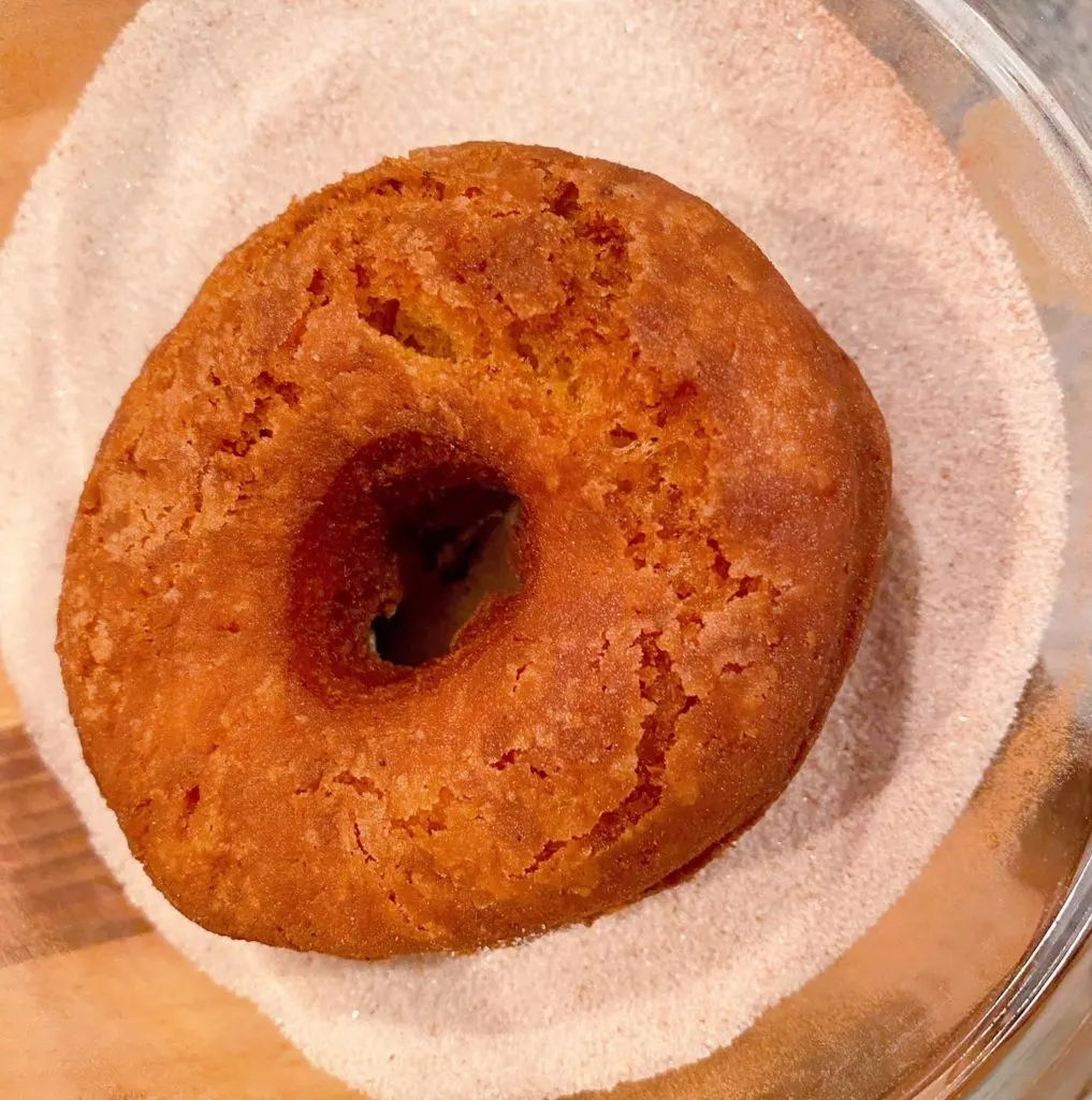 Dipping donut in cinnamon-sugar coating.