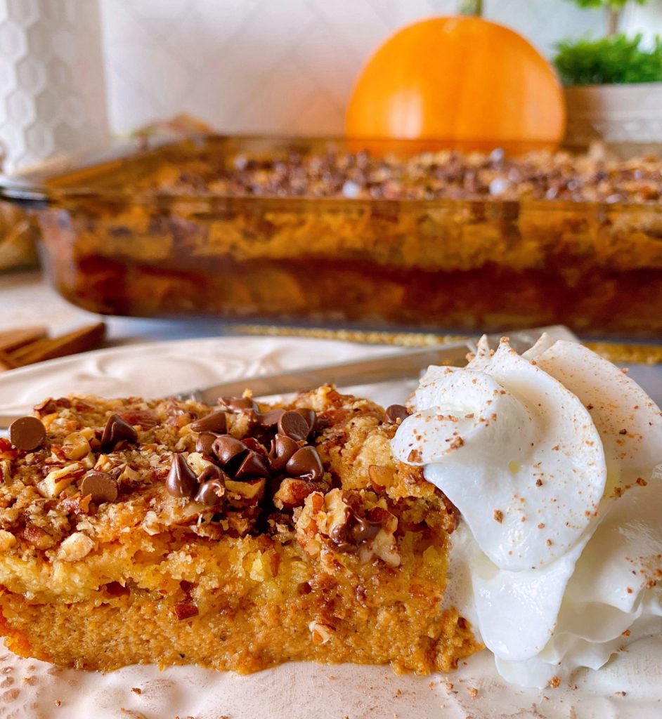 Pumpkin Chocolate Chip Dump Cake in the baking dish in the background, in front is a piece of pumpkin dump cake with whipped cream on a dessert plate.