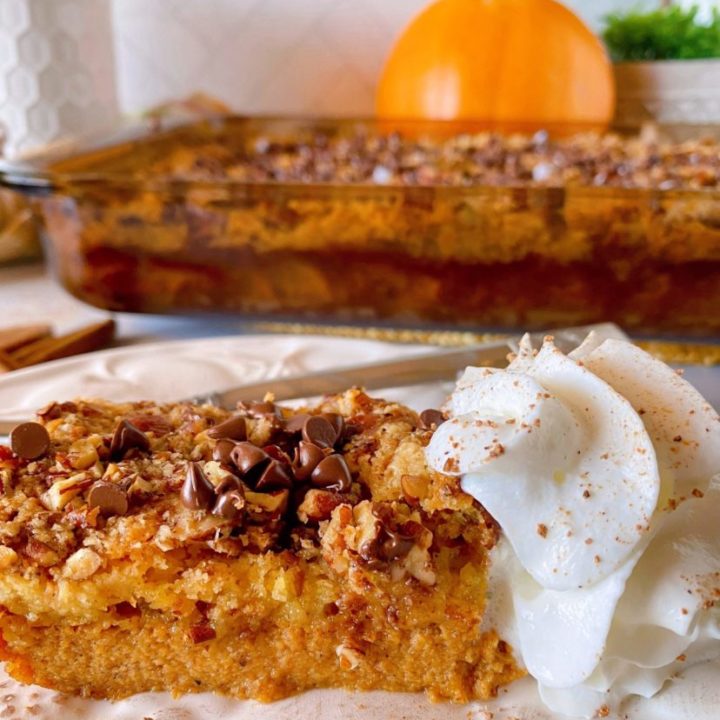 Pumpkin Chocolate Chip Dump Cake in the baking dish in the background, in front is a piece of pumpkin dump cake with whipped cream on a dessert plate.