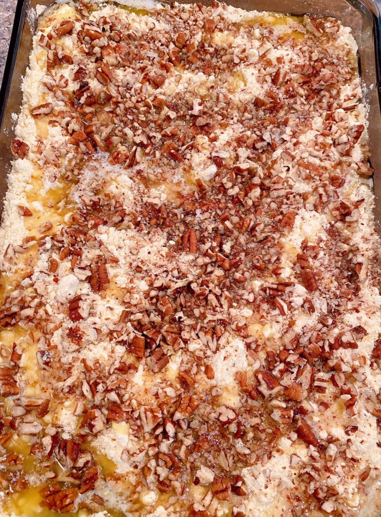 Pumpkin filling sprikled with cake mix and pecans and drizzled with butter ready for the oven.