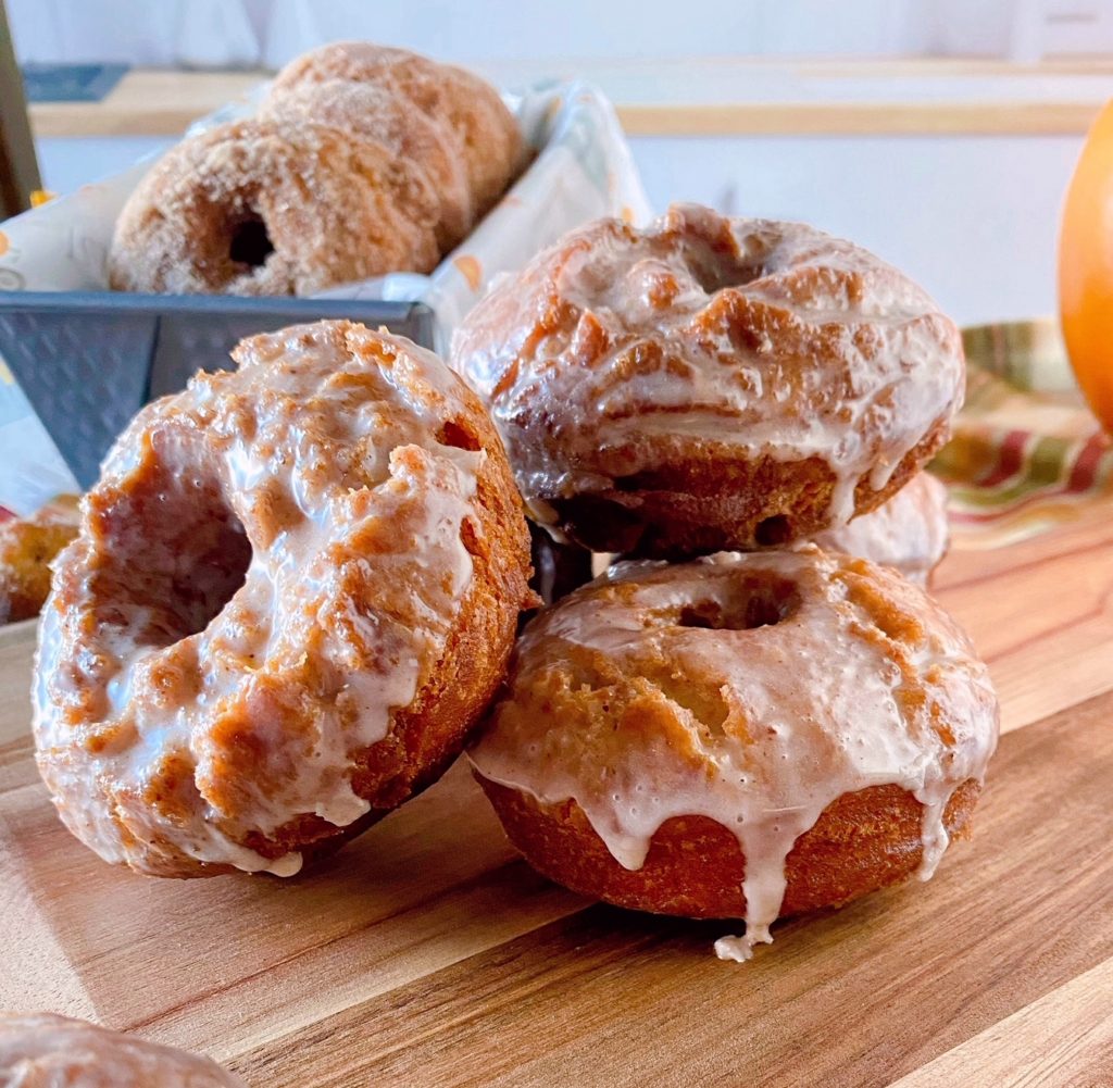 Pumpkin Spice Donuts on a cutting board with glaze dripping down them.