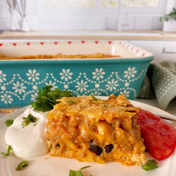 Breakfast Ranchero Egg Bake Casserole with a large serving on a plate surrounded by sour cream and freshly sliced tomatoes.