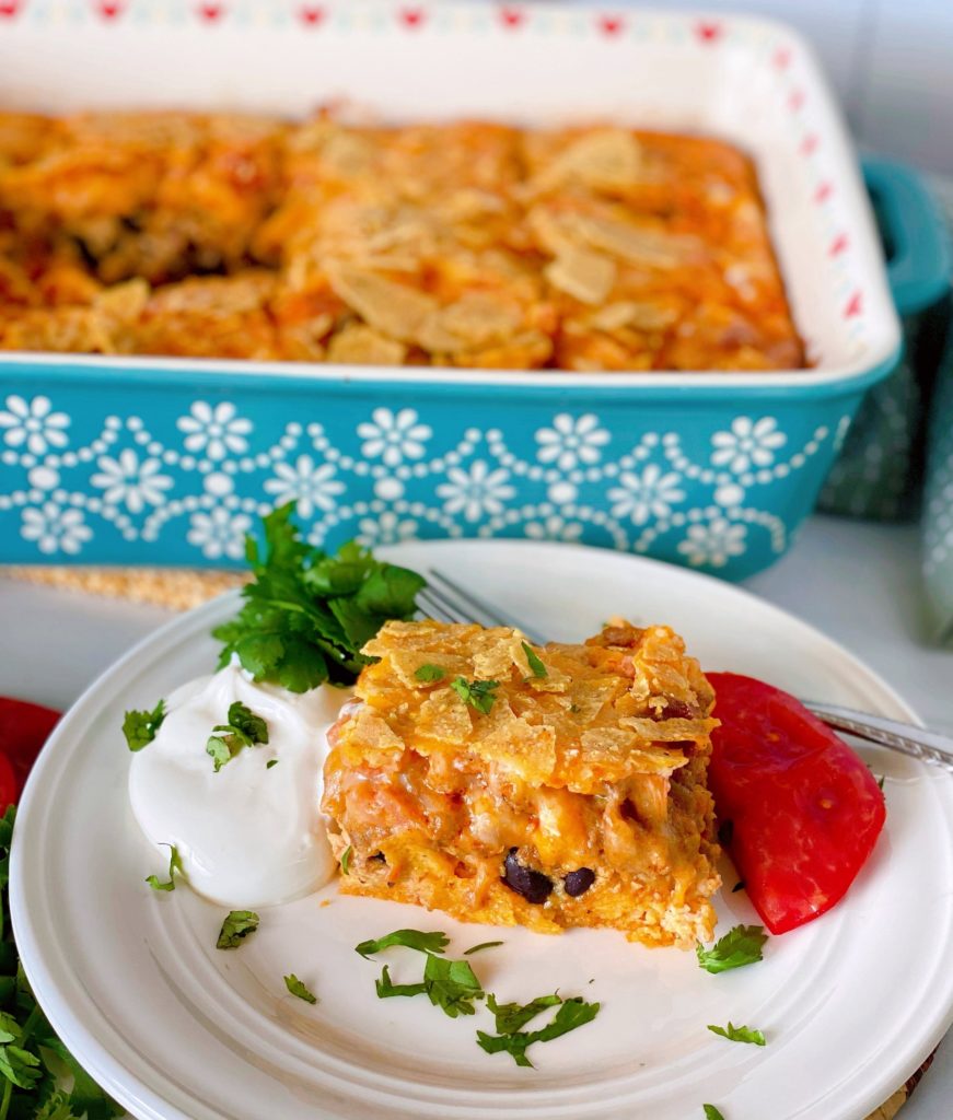 Breakfast Ranchero Egg Bake Casserole in a baking dish in the background with a single serving on a plate in front of the baking dish garnished with sour cream and tomatoe.