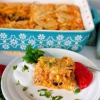 Breakfast Ranchero Egg Bake Casserole in a baking dish in the background with a single serving on a plate in front of the baking dish garnished with sour cream and tomatoe.