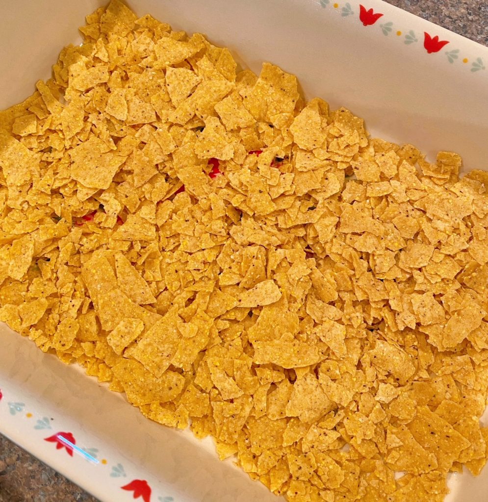 Spreading broken taco shells in bottom of baking dish.