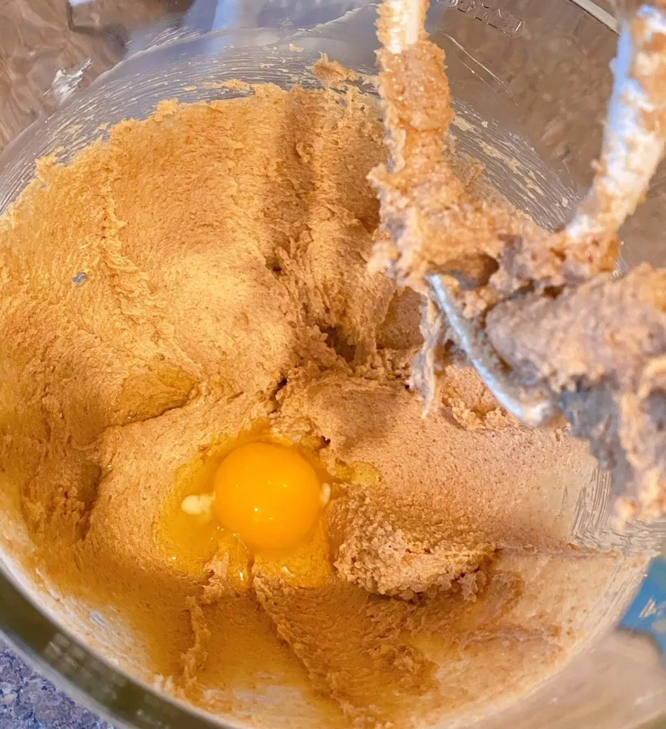 Adding egg to creamed butter and sugar in mixing bowl.