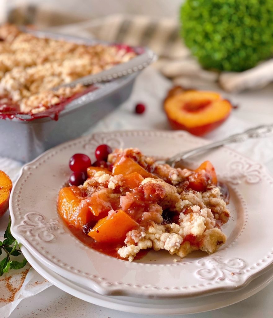 Cranberry Peach Cobbler served up on a plate with cobbler in baking dish in the background.