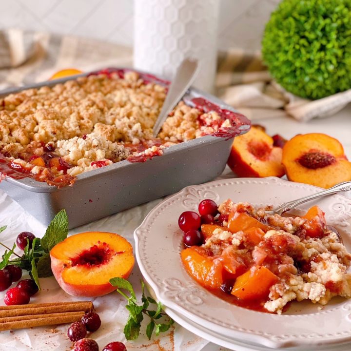 Peach Cranberry Cobbler in baking dish with a spoon in the background and a plate filled in the front with the dessert.