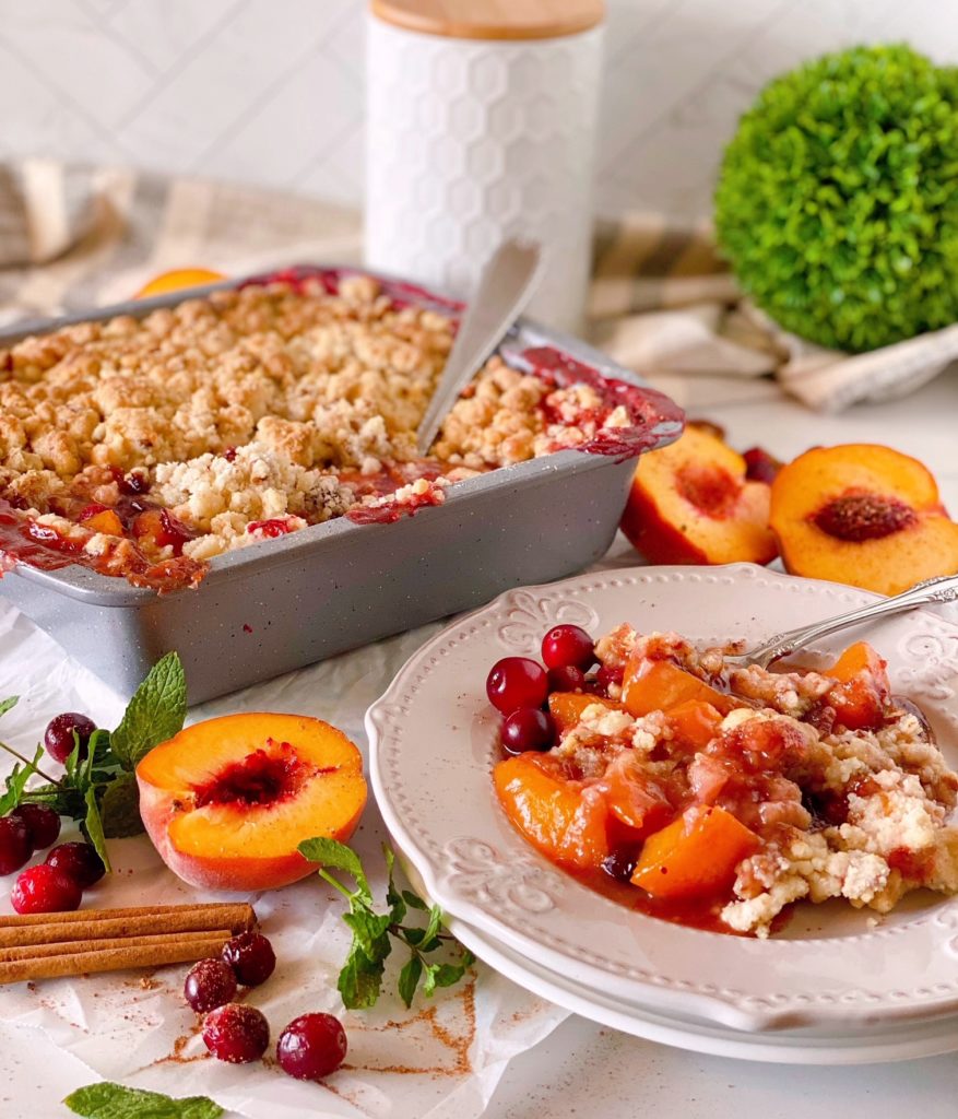 Peach Cranberry Cobbler in baking dish with a spoon in the background and a plate filled in the front with the dessert.