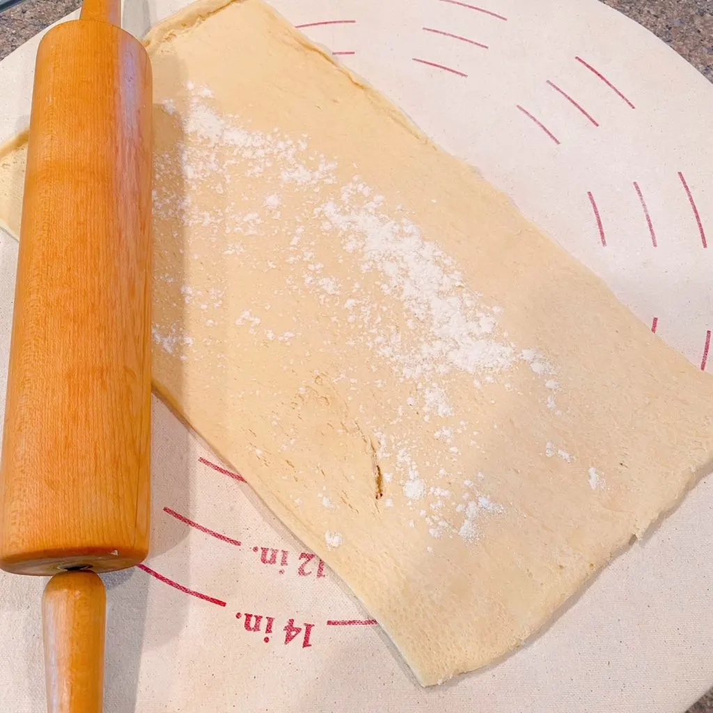 One sheet of crescent roll dough on a floured dough disc with a rolling pin.